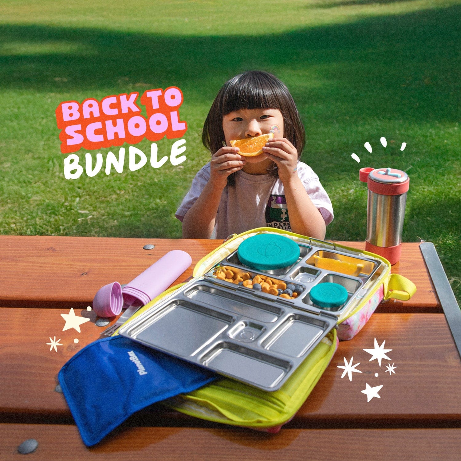Child eating outdoors with a lunch bundle on a wooden table, grass background