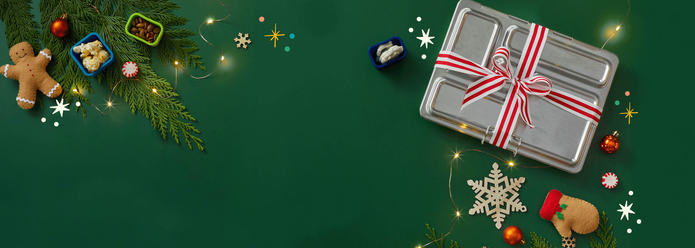 Decorative Christmas scene with a Rover Lunch Box wrapped in a bow, ornaments, Rover pods filled with snack, and festive lights on a green background.
