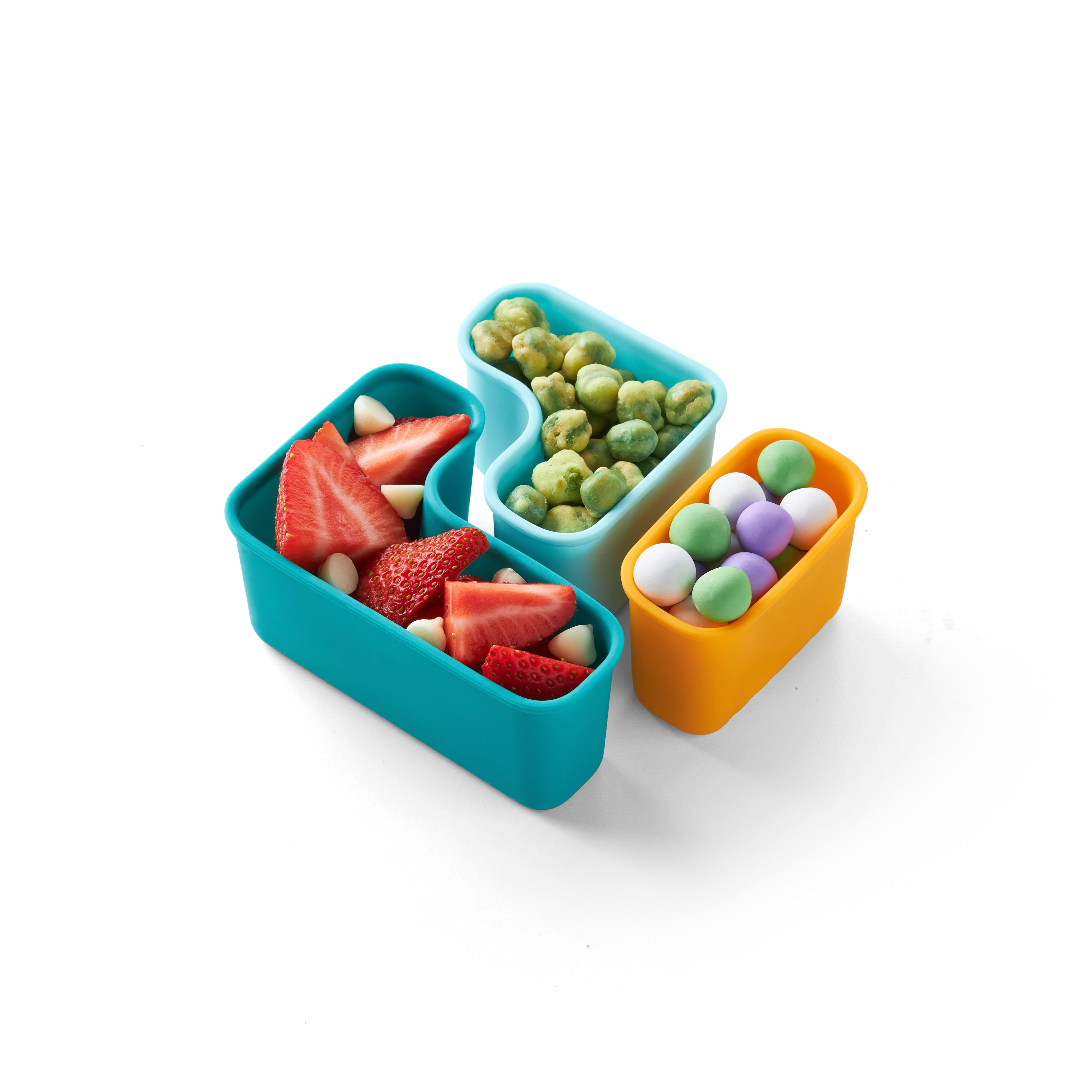 Teal, light blue and yellow puzzle pods on white background filled with strawberries, wasabi peas and pastel yogurt drops.
