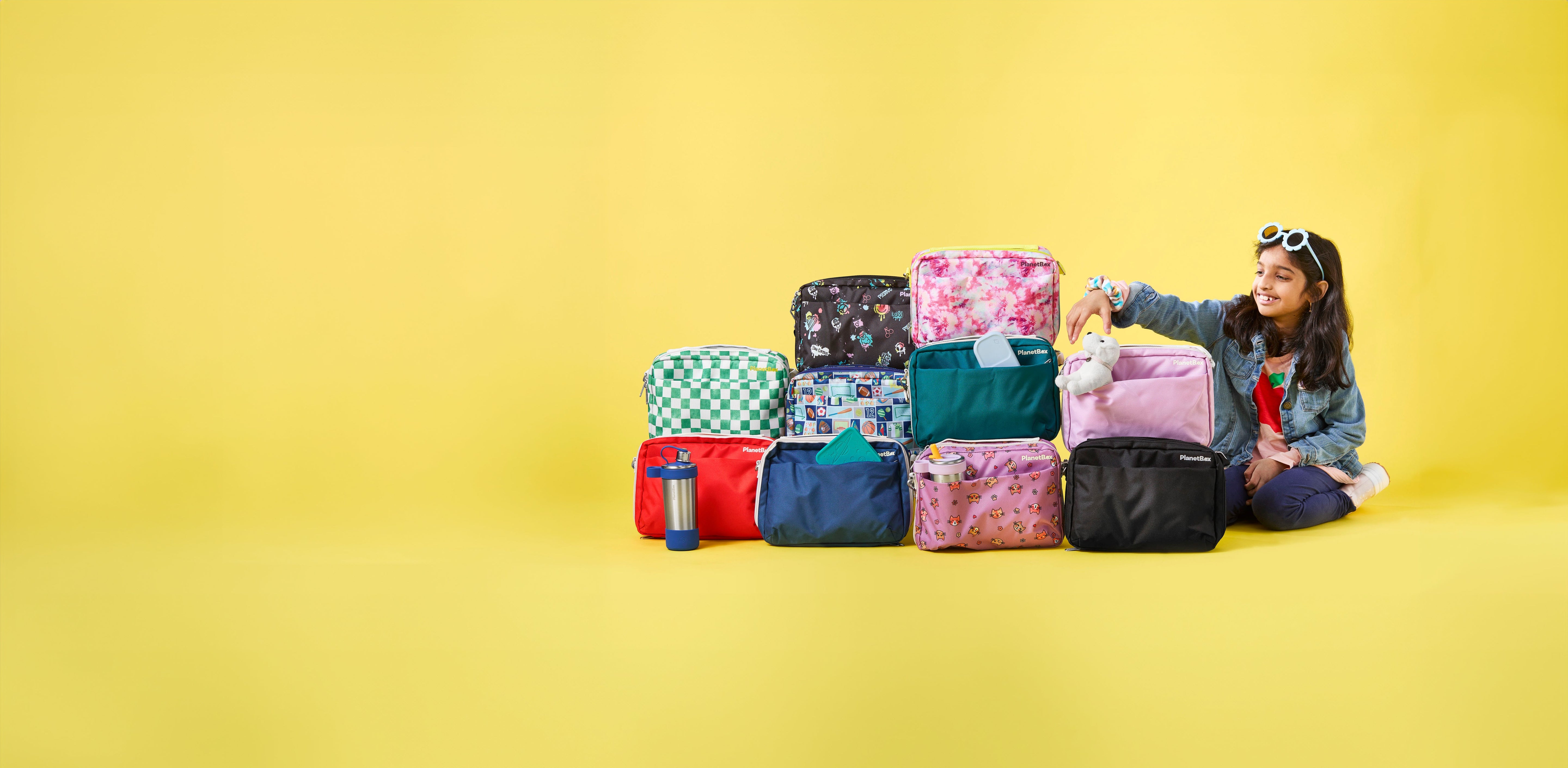 Assortment of PlanetBox lunch bags, including Slim Sleeve, and Carry Bags on a green background.