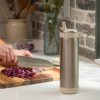 Stainless steel water bottle on a kitchen counter with a person chopping vegetables in the background.