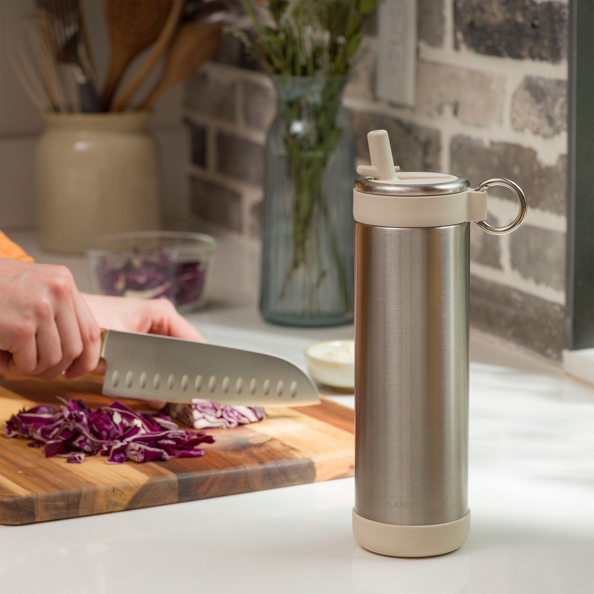 Stainless steel water bottle on a kitchen counter with a person chopping vegetables in the background.