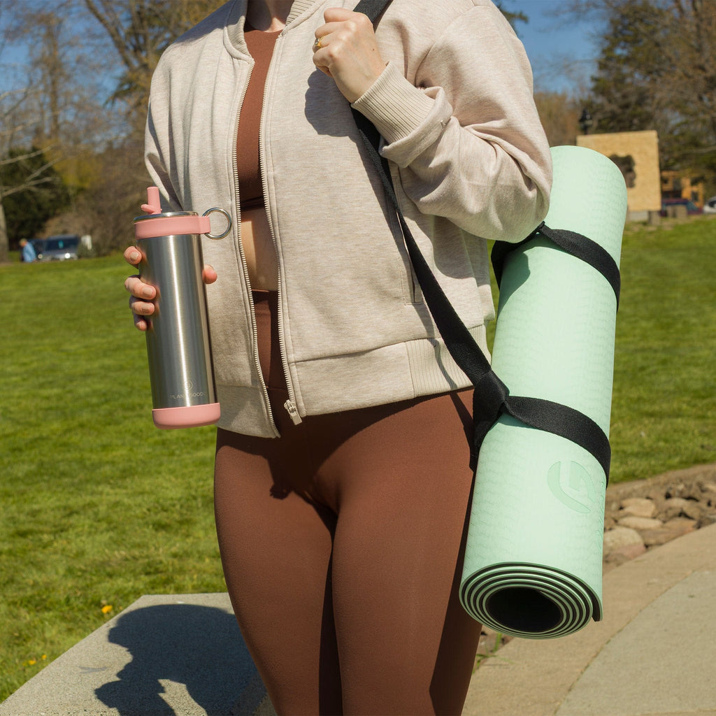 Person holding a water bottle and yoga mat outdoors