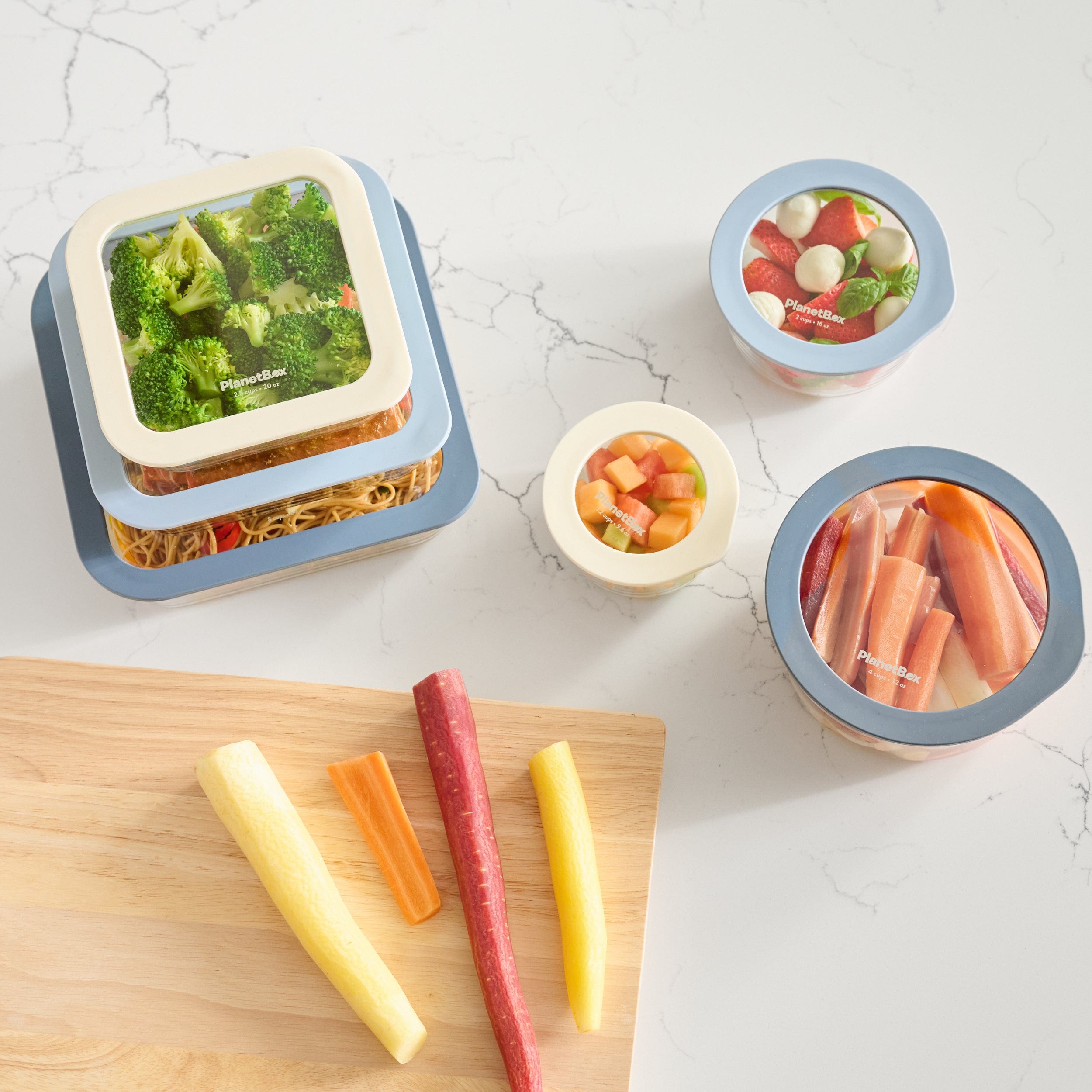 Set of glass containers on marble countertop alongside cutting board with carrots