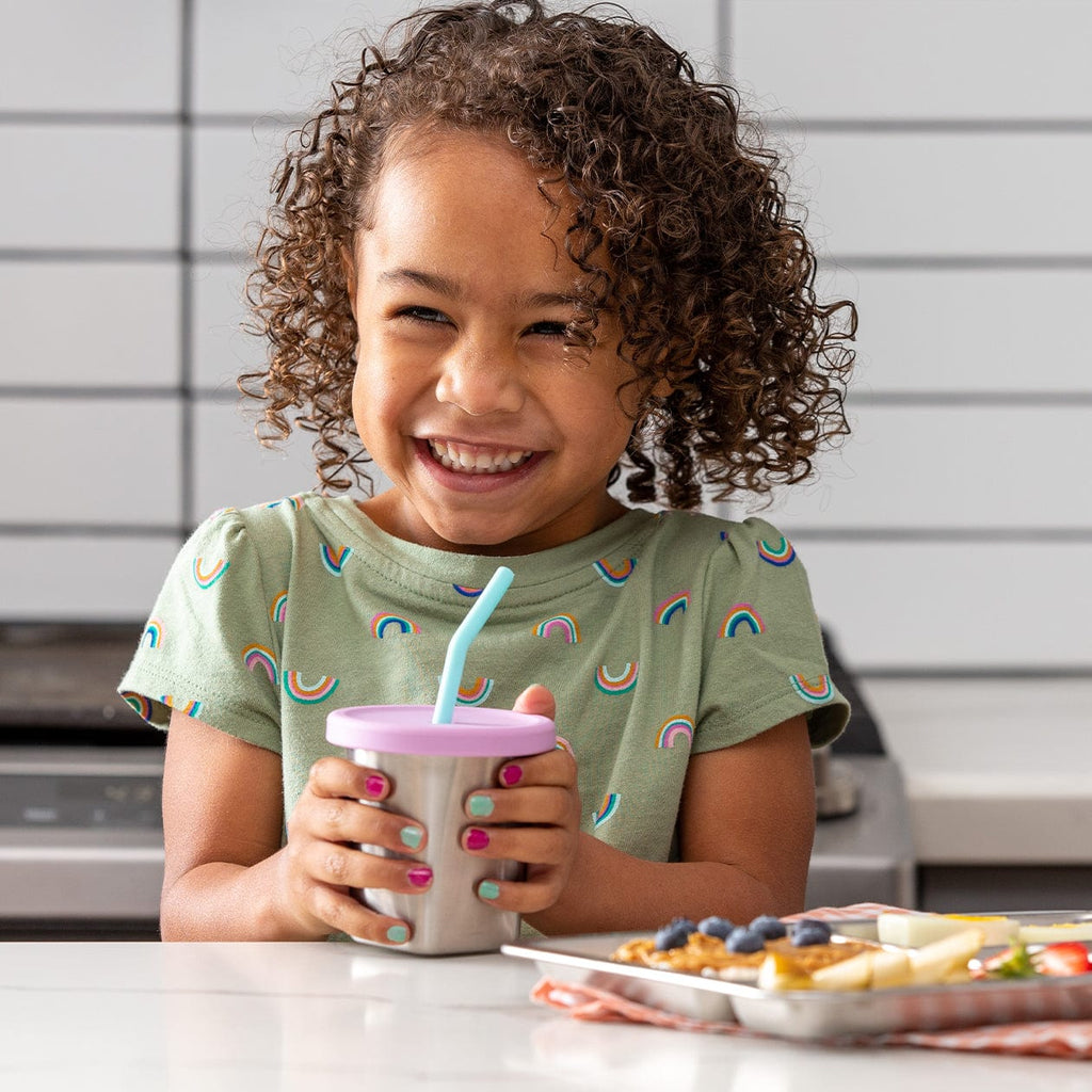 Young girl holding cup with purple silicone lid and blue straw. 
