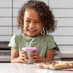 Young girl holding cup with purple silicone lid and blue straw. 
