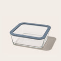 Square glass food storage container with blue lid holding a fresh salad with greens cucumbers and tomatoes.