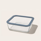 Square glass food storage container with blue lid holding a fresh salad with greens cucumbers and tomatoes.