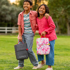 Two children laughing and holding lunchboxes in a field.
