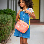 Young girl carrying the Small Carry bag across shoulder in front of a house.