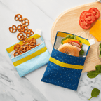 Snack packs in Ocean Dashes colorway opened with smaller one filled with pretzels spilling out, and larger one filled with a ham bagel sandwich. 